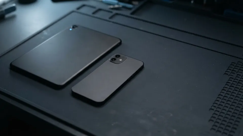 Small dark tablet and a smartphone lying face down together on a slate workbench mat