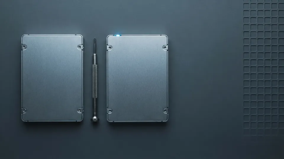 Two identical bare 2.5 inch drives side by side on a dark bench mat with a precision screwdriver between them, seen from overhead